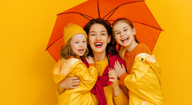 Eine Frau und 2 Junge glückliche Mädchen lachen mit orangen Regenschirm